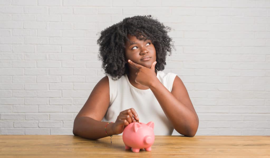 Black woman saving small amount of money in a piggy bank.